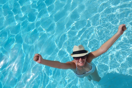 Happy smiling woman with hat and sunglasses  in swimming pool at tropical resort