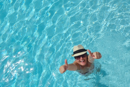 Happy smiling woman with hat and sunglasses  in swimming pool at tropical resort