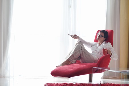 happy young woman relax at home on sofa in bright living room and watching tvの写真素材