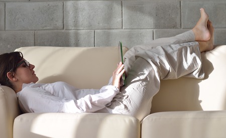 Young woman at home relaxing in her lliving room reading a digital tablet PC surf internet and workの写真素材