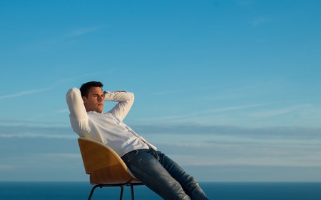 handsome young man relaxing and working on laptop computer at home balcony while looking sunsetの写真素材