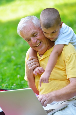 happy elderly senior grandfather and child in park using laptop computerの写真素材