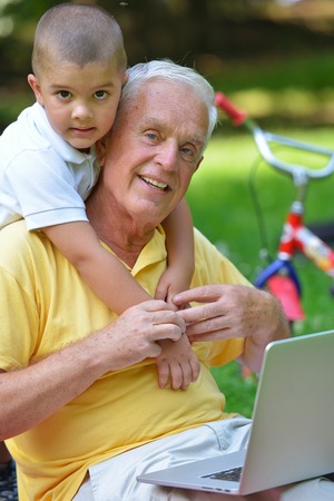 happy elderly senior grandfather and child in park using laptop computerの写真素材