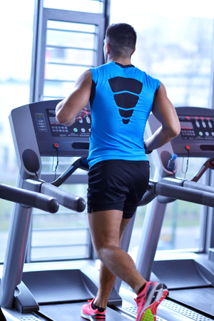 Handsome man running on the treadmill in modern gymの写真素材