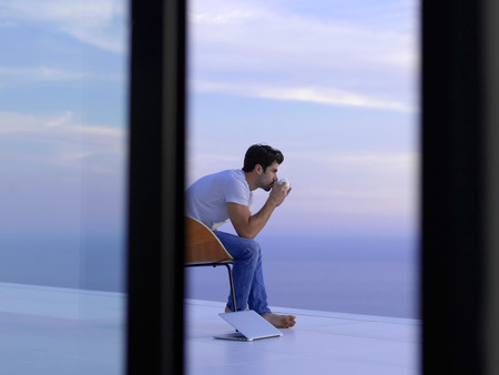 handsome young man relaxing and working on laptop computer at home balcony while looking sunset