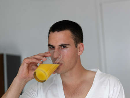 Happy man having orange juice with breakfast sitting at kitchen counterの写真素材