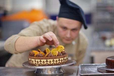 Closeup of a concentrated male pastry chef decorating dessert cake food in the kitchenの写真素材