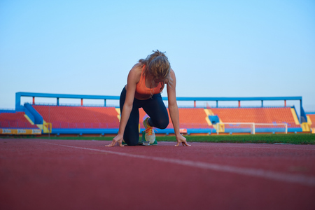 woman  sprinter leaving starting blocks on the athletic  track. Side view. exploding startの写真素材