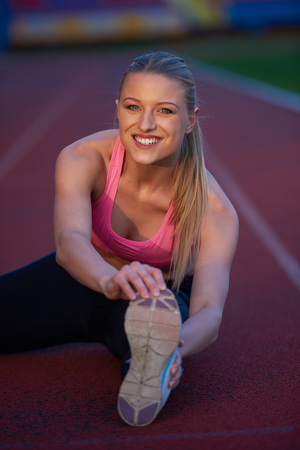 young runner sporty woman relaxing and stretching on athletic race trackの写真素材