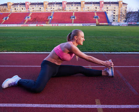 young runner sporty woman relaxing and stretching on athletic race trackの写真素材
