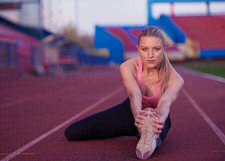 young runner sporty woman relaxing and stretching on athletic race trackの写真素材