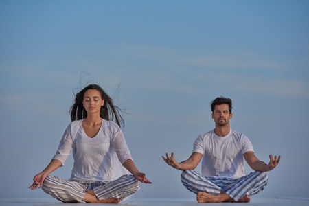 young couple practicing yoga at sunset in modern home terace with ocean and sunset in backgroundの写真素材