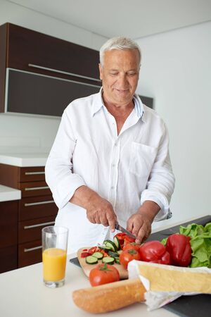 Handsome man cooking at home preparing salad in kitchen.の写真素材