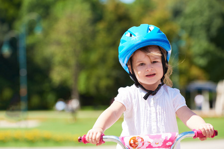 Cute smiling little girl with bicycle and helmet on road in the parkの写真素材