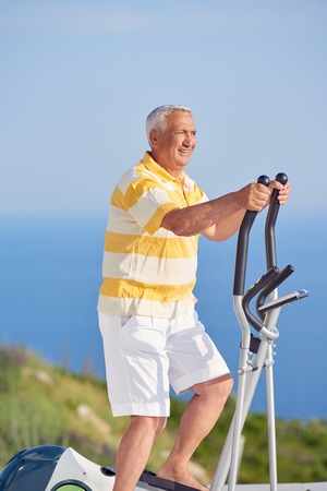 healthy senior man working out on gym treadmill machine at modern home terace with ocean viewの写真素材