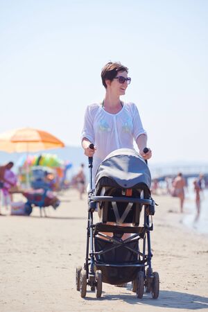 happy young mother walking on beach and push baby carriageの写真素材