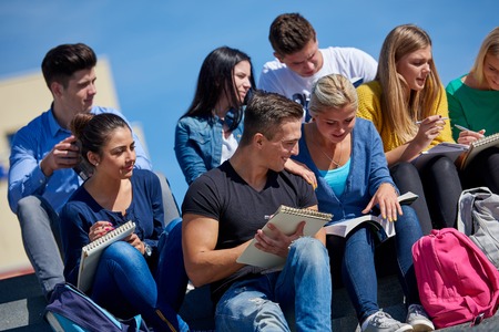 Group portrait  of happy  students outside in front of school sitting on steps have funの写真素材