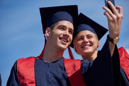 Capturing a happy moment.Students group  college graduates in graduation gowns  and making selfie photoの写真素材