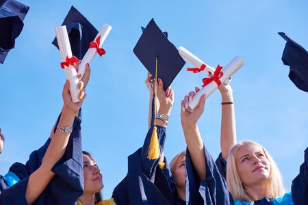 high school students graduates tossing up hats over blue sky.
