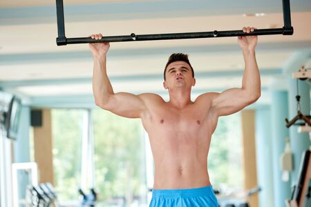handsome young man in fitness gym lifting up and hanging while working on hands and back muscles