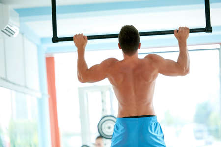handsome young man in fitness gym lifting up and hanging while working on hands and back muscles