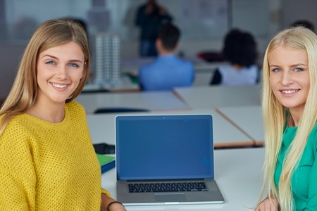 portrait of happy student girls together in classroom, laptop computer in background