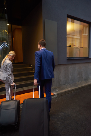 Young business people couple entering city  hotel, looking for room, holding suitcases while walking on streetの写真素材