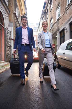Young business people couple entering city  hotel, looking for room, holding suitcases while walking on streetの写真素材