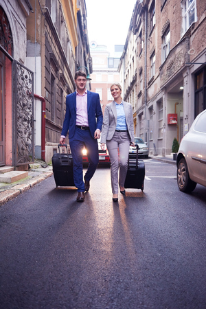 Young business people couple entering city  hotel, looking for room, holding suitcases while walking on streetの写真素材