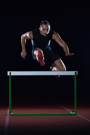 man athlete jumping over a hurdles on athletics race trackの写真素材