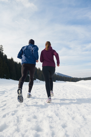 healthy young couple jogging outside on snow in forest. athlete running on  beautiful sunny winter dayの写真素材