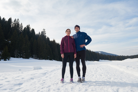 healthy young couple jogging outside on snow in forest. athlete running on  beautiful sunny winter dayの写真素材