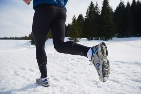 young  man jogging on snow in forest, bautiful sunny winter day. handsome sporty ahtlete man running