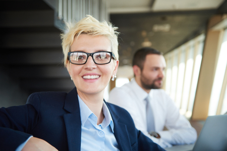 blonde with short hairstyle  and glasses,  business woman on meeting, people group in background at modern bright office indoorsの写真素材