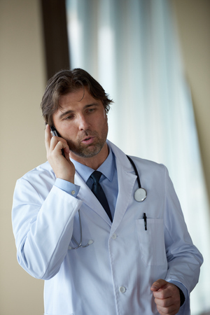 handsome doctor speaking on cellphone at modern hospital indoorsの写真素材