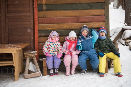 group portrait of kids, little child  group sitting together  in front of wooden cabin on vacation at beautiful winter  day with fresh snowの写真素材