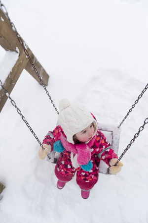 child outdoor in park at winter day with fresh snow, cute little girl swing and playingの写真素材
