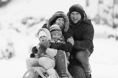 happy young family portrait on winter vacation while sitting sledge at  landscape with fresh falling snowの写真素材