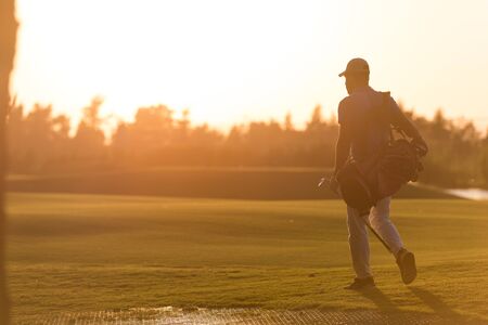 handsome middle eastern golfer  carrying  bag  and walking  to next hole at golf  course on beautiful sunset in backgroundの写真素材