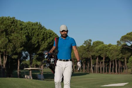 handsome middle eastern golfer  carrying  bag  and walking  to next hole at golf  courseの写真素材