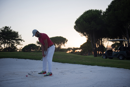 golf player shot ball from sand bunker at course with beautiful sunset with sun flareの写真素材
