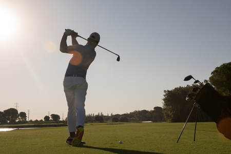 golf player hitting shot with club on course at beautiful morning with sun flare in backgroundの写真素材