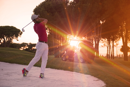 golf player shot ball from sand bunker at course with beautiful sunset with sun flareの写真素材