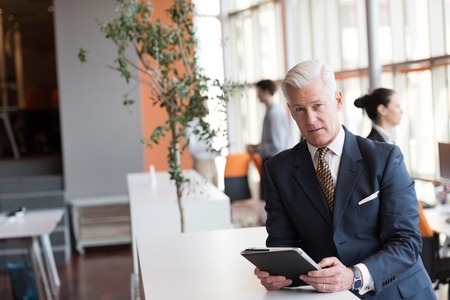 handsome senior business man with grey hair working on tablet computer at modern bright office interiorの写真素材