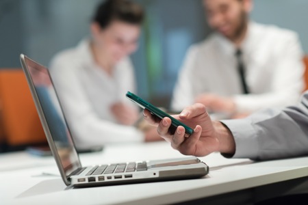 close up of  businessman hands  using smart phone and laptop computer, people group in office meeting  room blurred in backgronudの写真素材