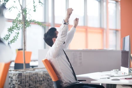 happy young business man  working on desktop computer at his desk in modern bright startup office interiorの写真素材