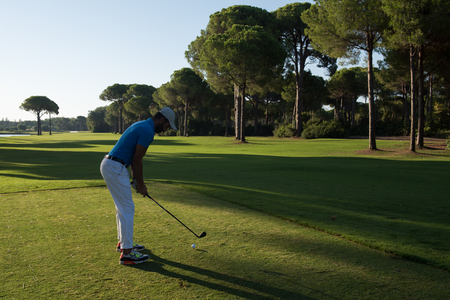 golf player hitting shot with club on course at beautiful morning with sun flare in backgroundの写真素材