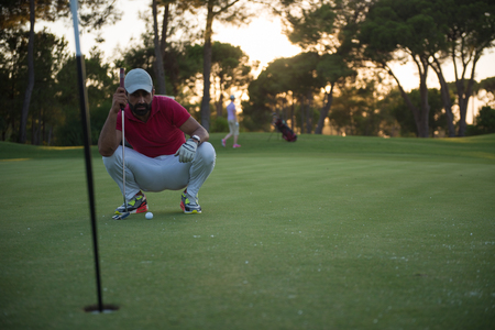 golf player aiming shot with club on course at beautiful sunset with sun flare in backgroundの写真素材