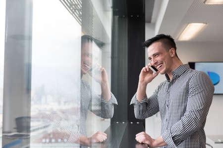 relaxed young businessman speaking on smart phone at modern startup business office meeting room  with big window and city in backgronudの写真素材
