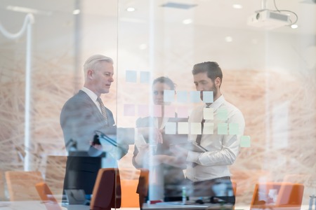 young creative startup business people on meeting with older senior mature businessman at modern office making plans and projects with post stickers on glassの写真素材
